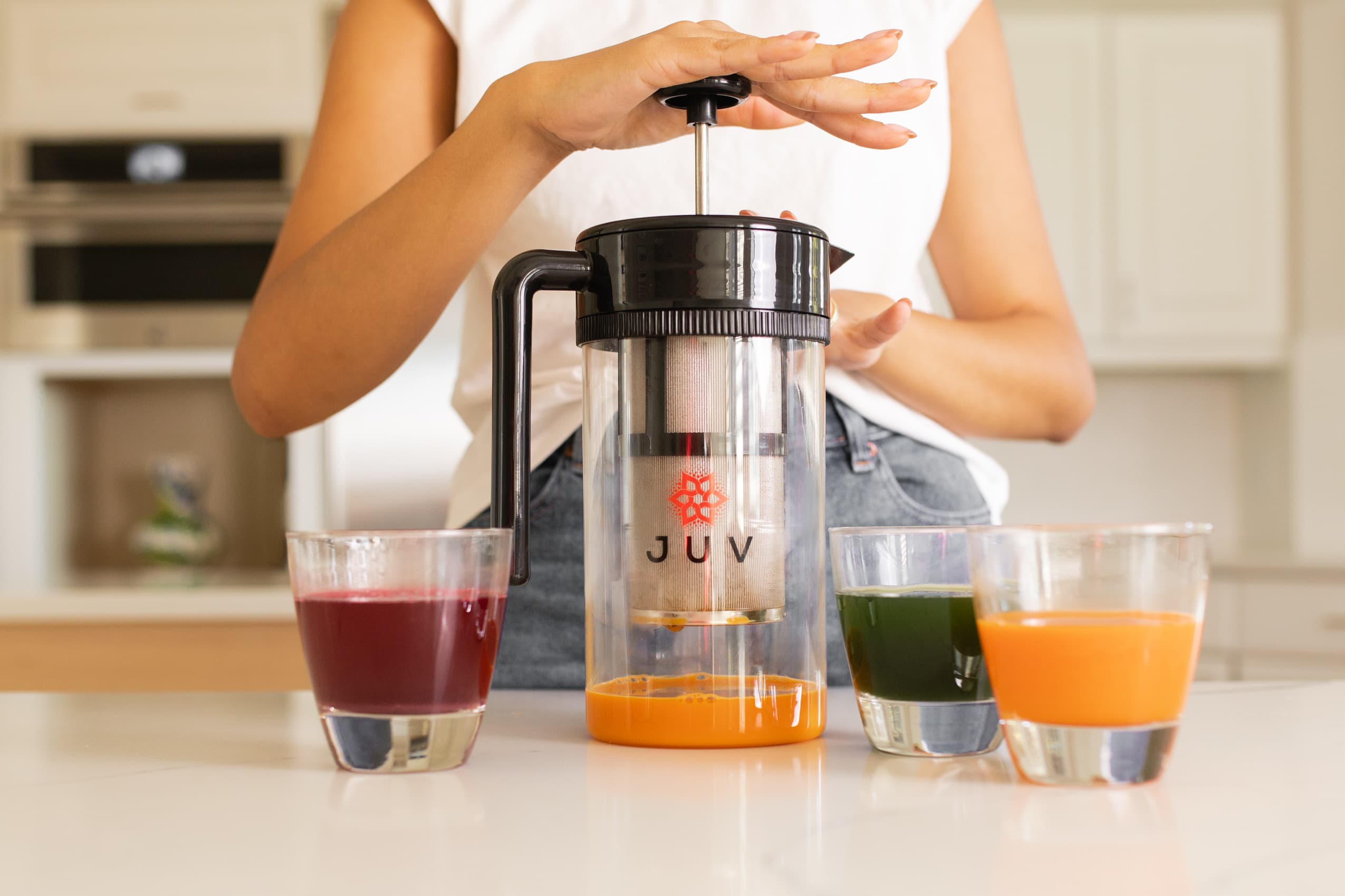 JUV Press with woman making orange juice with green and beet juices in glasses beside the JUV Press